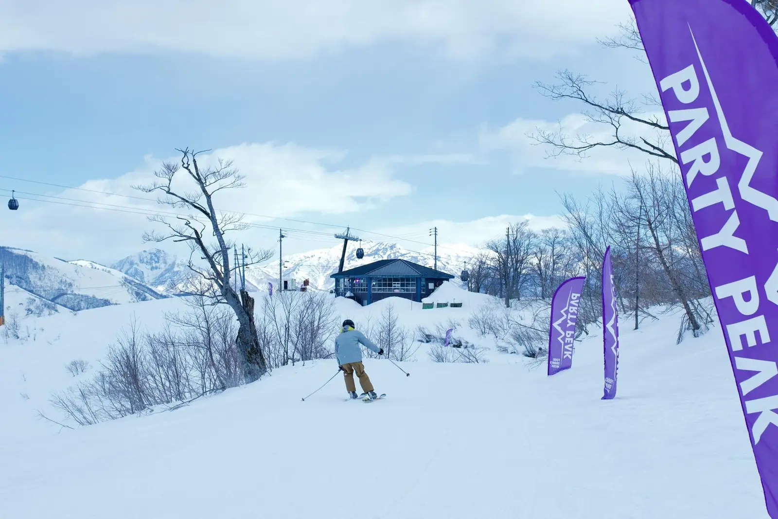 A skier riding down past the Party Peak flags toward the venue