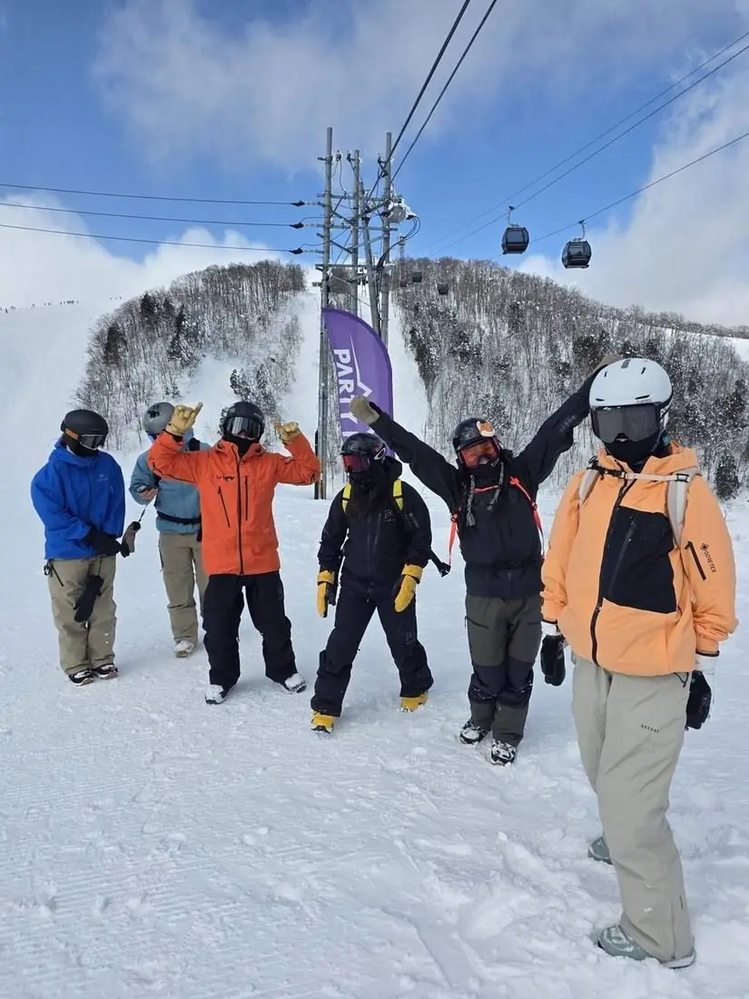 A group posing on the piste with the Party Peak flag behind