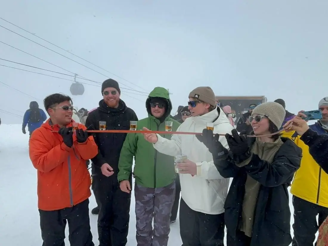 A group lined up taking a shot off a ski on the piste